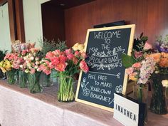 there are many vases with flowers on the table and a sign that says welcome to the flower bar