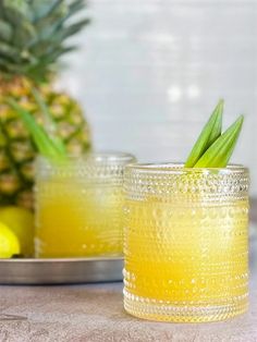 two glasses filled with yellow liquid next to a pineapple