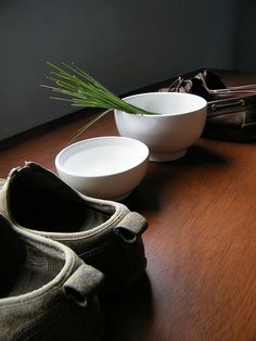 two white bowls sitting on top of a wooden table next to a bag and purse