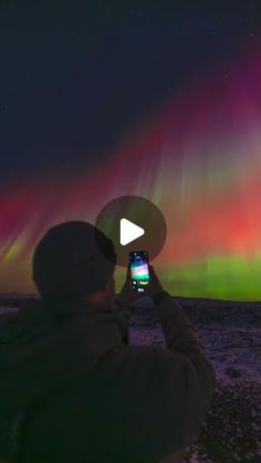 a person holding up a cell phone in front of an aurora display