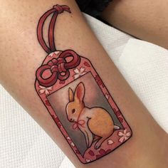 a woman's leg with a tattoo on it and a tag that has an image of a rabbit inside