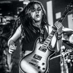 a woman with long hair holding a guitar in front of a microphone and drum set