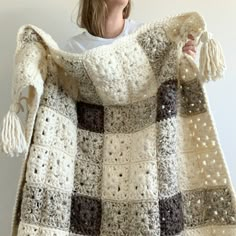 a woman is holding up a crocheted blanket