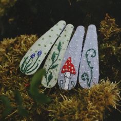 three hand - embroidered bookmarks sitting on top of some moss covered ground with plants and mushrooms