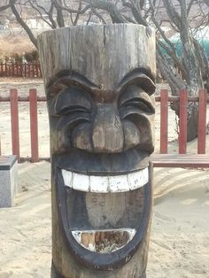 a carved wooden totem sitting on top of a sandy beach next to a tree