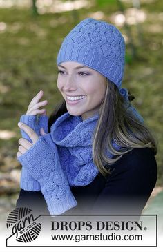 a woman wearing a blue knitted hat and scarf with her hands in the air