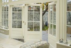 a living room filled with lots of windows next to a stone wall and white furniture