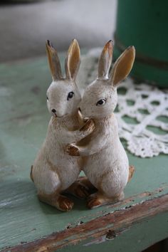 two small figurines sitting on top of a green table next to a doily