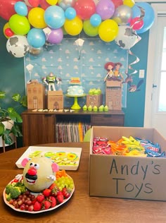 a birthday party with balloons, cake and fruit on the table in front of it