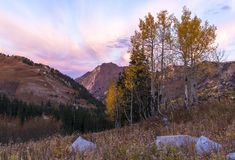 the sun is setting in the mountains with some trees and rocks on the ground below