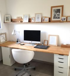 a desk with a computer and some pictures on the wall above it in a home office