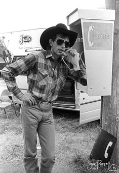 black and white photograph of man in cowboy hat leaning against telephone pole with cell phone