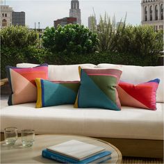 a couch with colorful pillows on top of it next to a table and some drinks