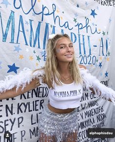 a woman wearing a white shirt and silver skirt posing for a photo in front of a banner