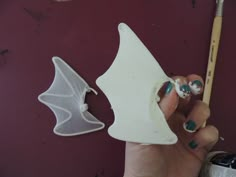 a hand holding a white bat shaped object next to a paintbrush and some other items