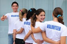 a group of young people standing next to each other in front of a building with volunteer t - shirts on