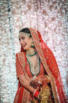 a woman in a red and gold bridal outfit with jewelry on her head, smiling