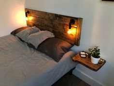 a bed that has some lights on the headboard and pillows in front of it