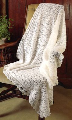 a white crocheted blanket sitting on top of a chair next to a potted plant