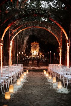 rows of white chairs lined up in an archway with lit candles at the end and on each side