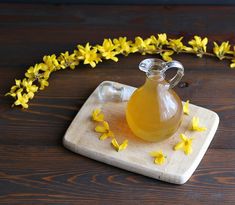 a glass jug filled with liquid sitting on top of a cutting board next to yellow flowers