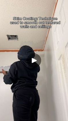 a man is painting the ceiling with white paint and black sweatpants, while holding a brush in his hand