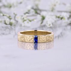 a gold ring with a blue stone in the center on a white surface surrounded by flowers