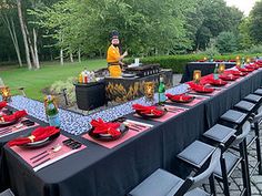 a long table set up with red plates and black napkins for an outdoor party