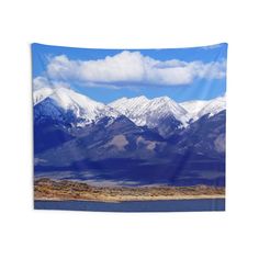 the mountains are covered in snow and blue sky with clouds above them, as seen from across the lake