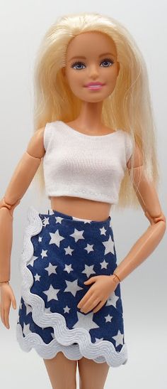 a doll with blonde hair wearing a blue skirt and white cropped top is standing in front of a white background