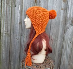 "Style: Chunky slouchy bonnet style hat with braided ties and large pom pom. Color: This sample hat is shown in Pumpkin. Sizes: One size fits average teen or adult head size of 20\" to 23\" (50.5 cm to 58 cm). Fiber Content: 80% acrylic, 20% Wool Characteristics: Chunky, very soft, warm and cozy. Care Instructions: Hand wash, dry flat. Every item from Pixiebell is handmade and knit or crocheted to order, unless otherwise stated in title of the item as \"ready to ship\". Production time may vary, Orange Beanie, Crochet 101, Orange Hat, Mens Beanie Hats, Flap Hat, Womens Hats, Chunky Knit Hat, Ear Flap Hats, Pixie Hat