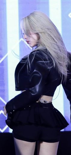 a woman with long blonde hair wearing a short skirt and black leather jacket on stage