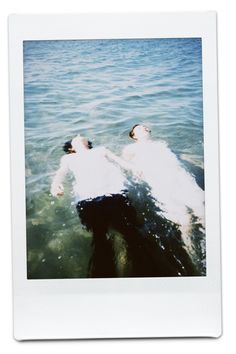 two people laying on their back in the water with one person wearing a white shirt and black pants