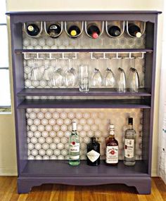 a purple shelf with wine glasses and bottles on it in front of a white wall