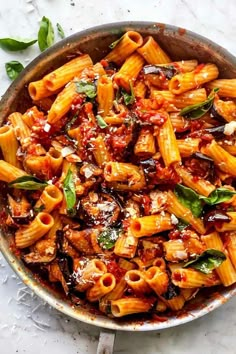 a pan filled with pasta and sauce on top of a white tablecloth next to a knife