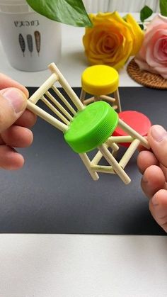 two hands holding small wooden chairs with plastic caps on them and flowers in the background