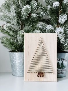 a small wooden christmas tree on a table next to a potted plant with pine cones