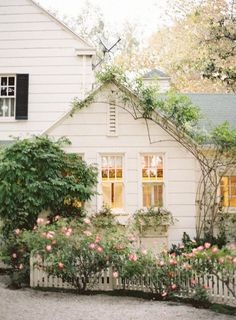 a white house with pink flowers in front of it and a picket fence around it