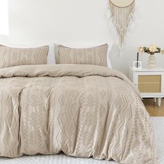 a bed with beige comforter and pillows in a bedroom next to a white nightstand