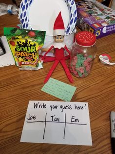 an elf is sitting on the table with his name written in front of him and some candy