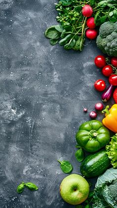 an assortment of fruits and vegetables laid out on a gray surface with space for text