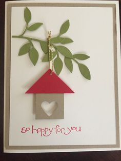 a handmade card with a birdhouse and heart hanging from the top, on a table