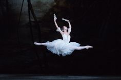 a ballerina in the air with her arms outstretched and legs spread out, while she is wearing a white tutu