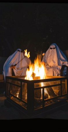 two white cloths wrapped around an open fire pit in the dark, with flames burning behind them