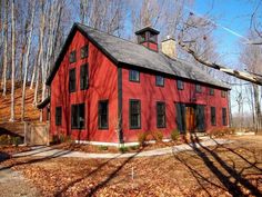 a red house in the woods with lots of leaves on the ground and trees around it