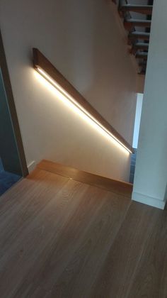 an illuminated stair case in the corner of a room with wood floors and white walls