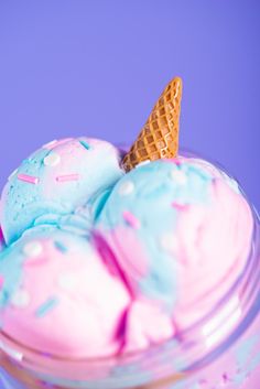 two scoops of ice cream with sprinkles in a glass container on a purple background