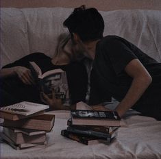 a man laying on top of a white couch next to stacks of book's