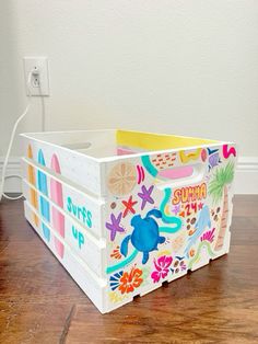 a white box with colorful designs on it sitting on top of a wooden floor next to a wall