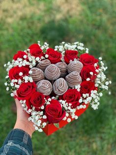 a heart shaped box filled with chocolates and red roses in someone's hand